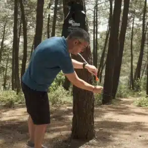 Mann wäscht sich die Hände mit der Urban Badger Campingdusche 20L, die an einem Baum im Wald aufgehängt ist.