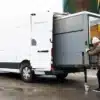 Frau schiebt ein großes Camper-Modul auf Rollen in einen weißen Transporter.