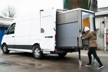 Frau schiebt ein großes Camper-Modul auf Rollen in einen weißen Transporter.