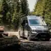 Der Aquila Adventure Creston Crafter 4x4 fährt auf einer schlammigen Waldstraße zwischen gefällten Baumstämmen.