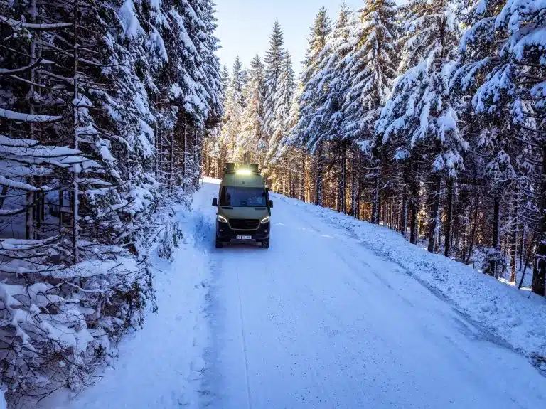 Aquila Adventure Sprinter Stenar 4x4 auf schneebedeckter Waldstraße zwischen verschneiten Bäumen.