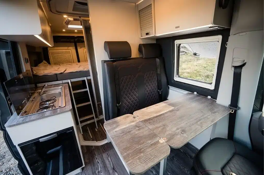 Innenansicht vom Aquila Adventure Sprinter Stenar 4×4 mit Sitzgruppe, Esstisch, Küche und Bett im Hintergrund