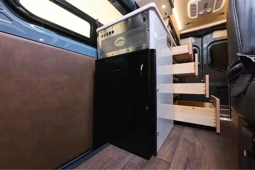 Küchenzeile des Beast Mode XO Campervans mit geöffneten Schubladen, Stauraum und Kühlschrank.
