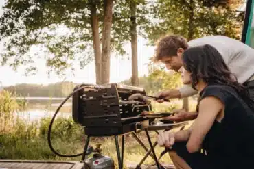 Zwei Camper grillen am See mit einem Berger 3-Flammen Koffergasgrill Schwarz im Freien.