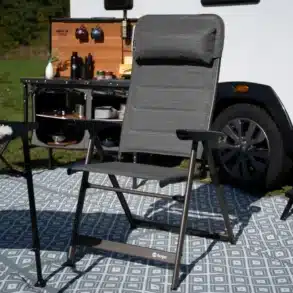 Berger Slimline Klappstuhl aufgeklappt auf Campingteppich vor Wohnmobil und mobilem Küchenmodul.