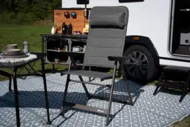 Berger Slimline Klappstuhl aufgeklappt auf Campingteppich vor Wohnmobil und mobilem Küchenmodul.