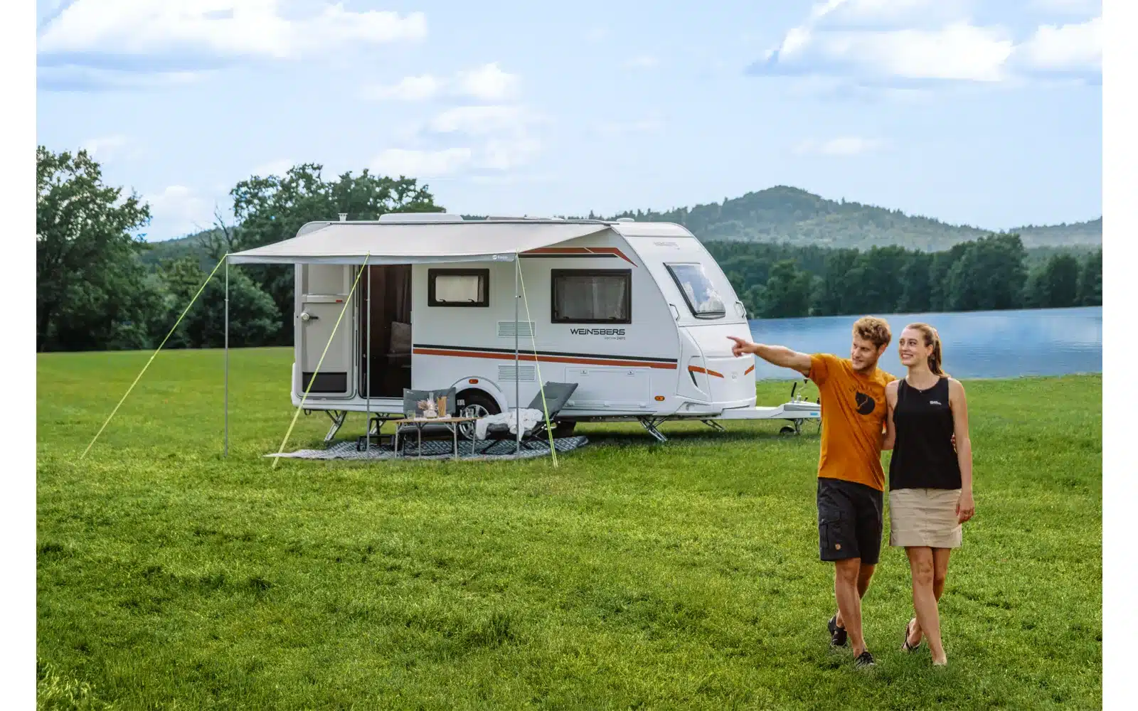 Wohnwagen mit Berger SunRoof Sonnenvordach und zwei Campern am See auf einer Wiese