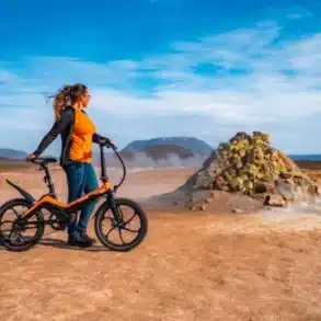 Frau mit orangefarbenem Blaupunkt Fiene faltbares E-Bike 20 Zoll vor landschaftlicher Kulisse.