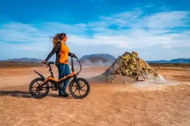 Frau mit orangefarbenem Blaupunkt Fiene faltbares E-Bike 20 Zoll vor landschaftlicher Kulisse.