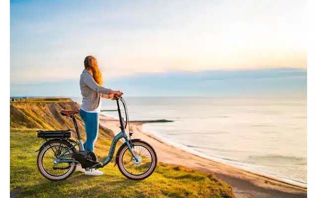 Frau mit Blaupunkt Franzi faltbarem E-Bike blickt aufs Meer, geeignet für Camper und Vanlife.