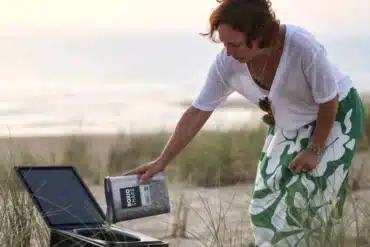 Frau befüllt eine BOXIO Trenntoilette im Freien am Strand mit Einstreu.