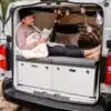 Mann liegt auf dem modularen Camper Lite Camping-Set im geöffneten Van und liest ein Buch.