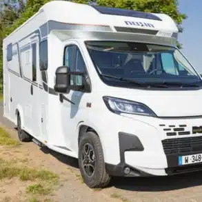Der Camping-Car Bilbao BCL, ein weißes teilintegriertes Reisemobil auf Fiat-Basis, steht auf einer Landstraße in ländlicher Umgebung.