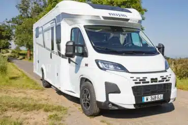 Der Camping-Car Bilbao BCL, ein weißes teilintegriertes Reisemobil auf Fiat-Basis, steht auf einer Landstraße in ländlicher Umgebung.