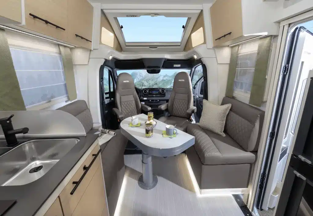 Wohnbereich und Sitzgruppe im Exclusiv Lindau JF Reisemobil, Mercedes Sprinter Basis, Camper Innenraum mit Tisch und Sitzen.