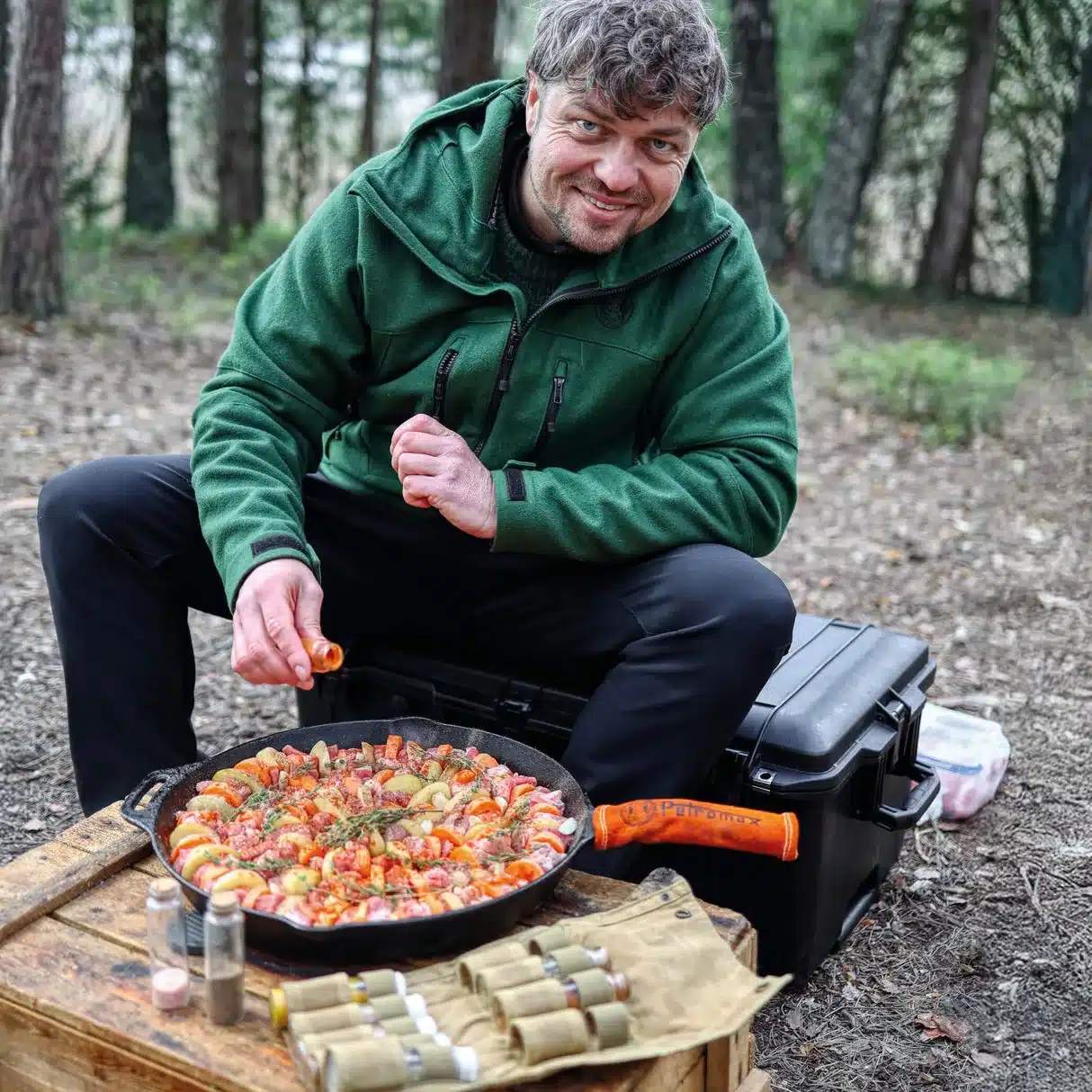Mann bereitet Essen in einer gusseisernen Petromax Feuerpfanne mit Stiel im Wald zu.