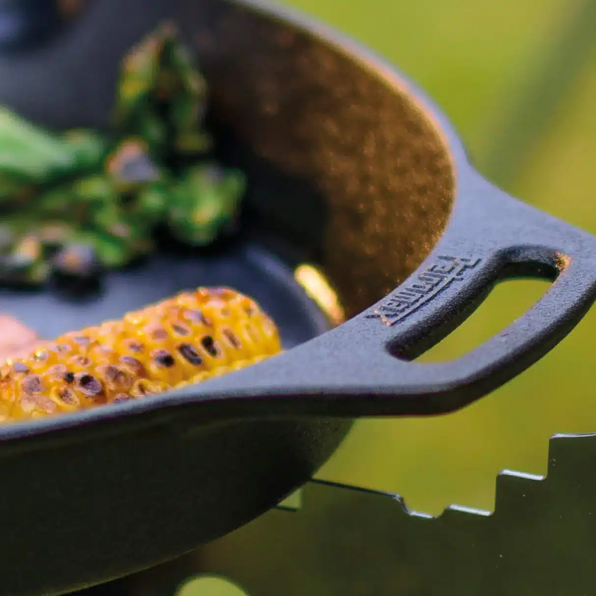 Nahaufnahme einer gusseisernen Feuerpfanne mit gegrilltem Gemüse und Maiskolben.