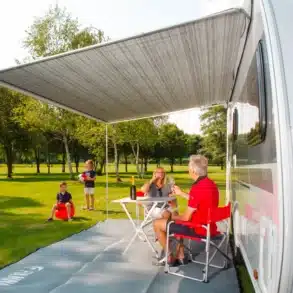Aufgespannte Fiamma Caravanstore XL Markise an einem Wohnwagen mit entspannten Campern darunter.