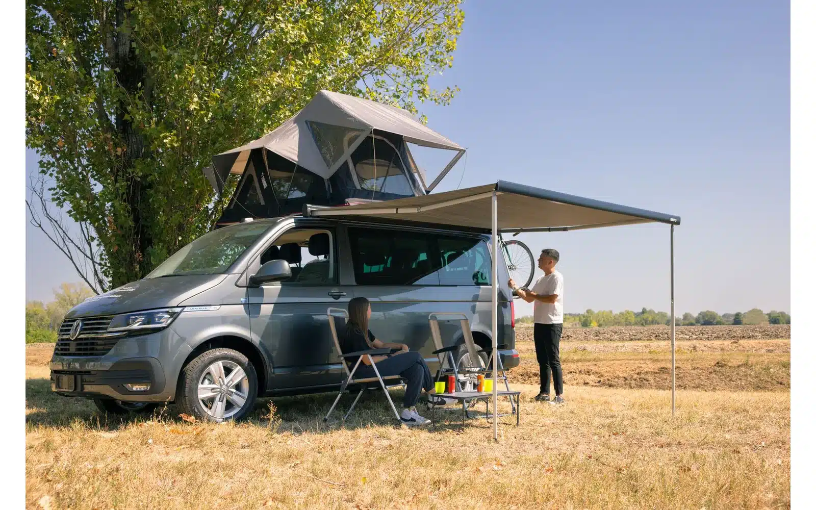 Campingbus mit Fiamma F43van Markise in geöffneter Position, Personen genießen den Schatten im Freien.