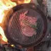Steak in einer gusseisernen Grill-Feuerpfanne auf offenem Lagerfeuer