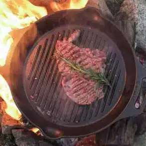 Steak in einer gusseisernen Grill-Feuerpfanne auf offenem Lagerfeuer