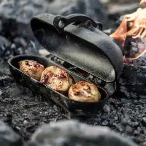 Gusseiserner Kartoffelbräter von Petromax, geöffnet am Lagerfeuer mit gebackenen Kartoffeln.