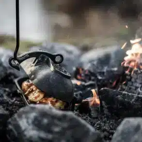 Offener gusseiserner Kartoffelbräter mit goldbraunen Kartoffeln am Lagerfeuer