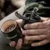 Hand hält eine Petromax Handkaffeemühle mit geöffnetem Bohnenbehälter und Gusseisen-Mahlwerk, gefüllt mit Kaffeebohnen.