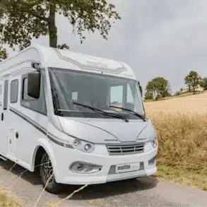 Weißes I.Progress Rubi CF Reisemobil steht auf einer schmalen Landstraße, umgeben von Feldern und Bäumen.