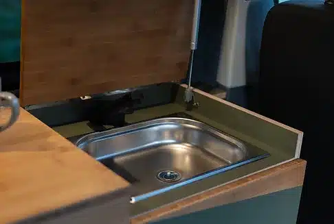 Edelstahlspüle mit aufgeklappter Glasabdeckung im Innenraum eines ausgebauten Campingvans