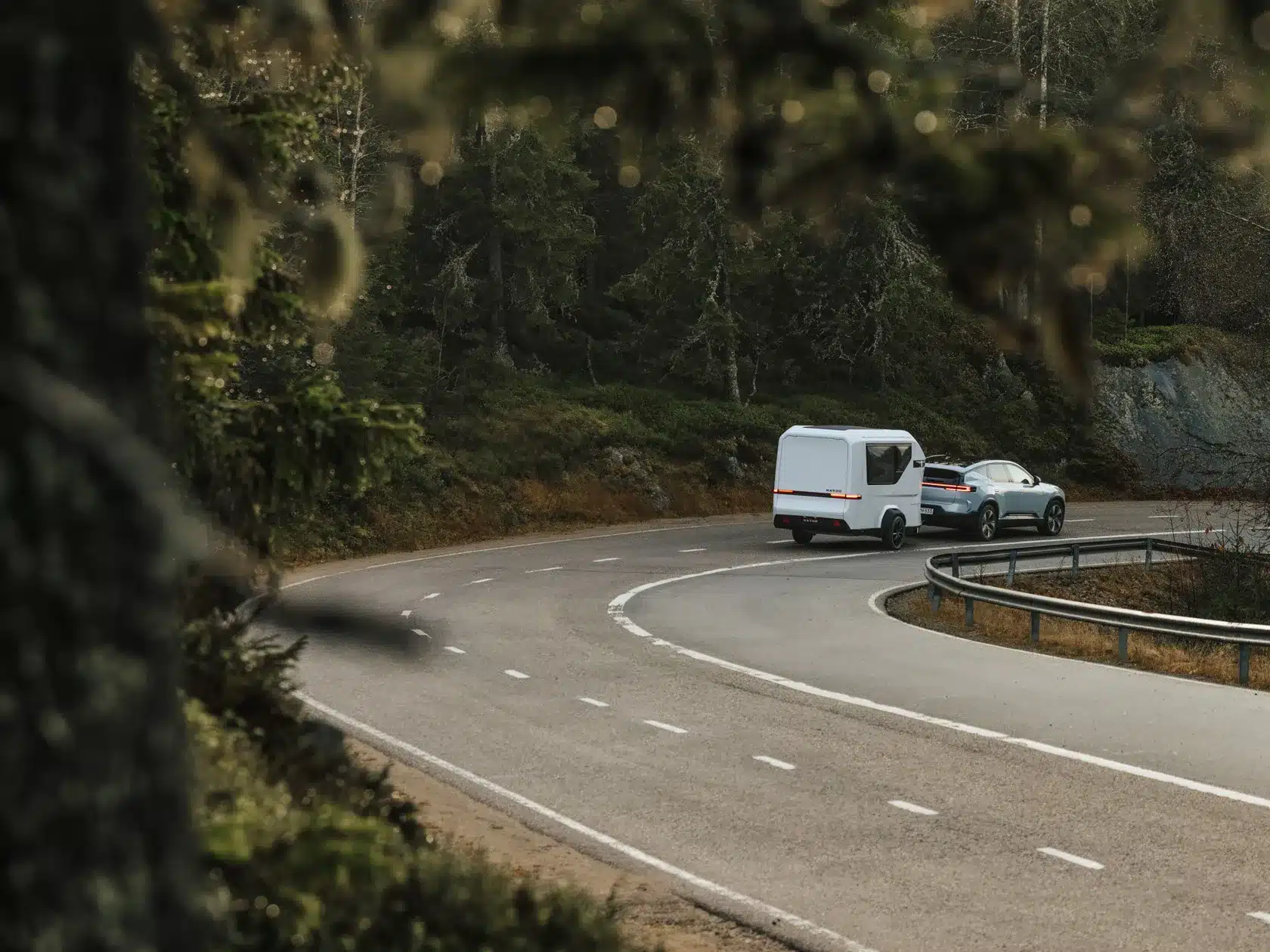 Karoo Camper Wohnwagen im modernen Design an einem Auto, unterwegs auf einer abgelegenen Straße in waldreicher Umgebung.