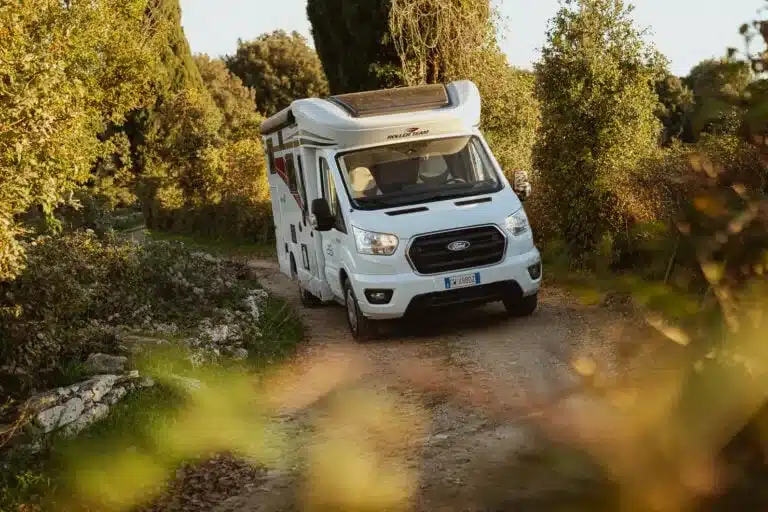 Kronos Fit Wohnmobil fährt auf einem schmalen Feldweg durch grüne Landschaft.
