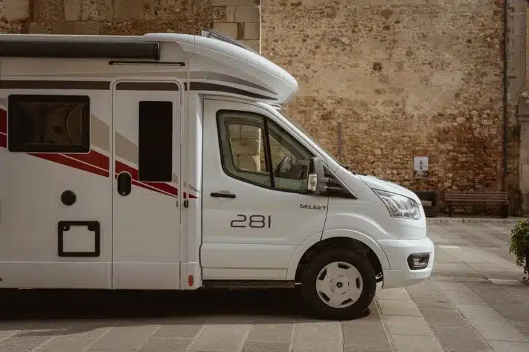 Kronos Fit 281 Wohnmobil seitlich geparkt vor einer Steinmauer.