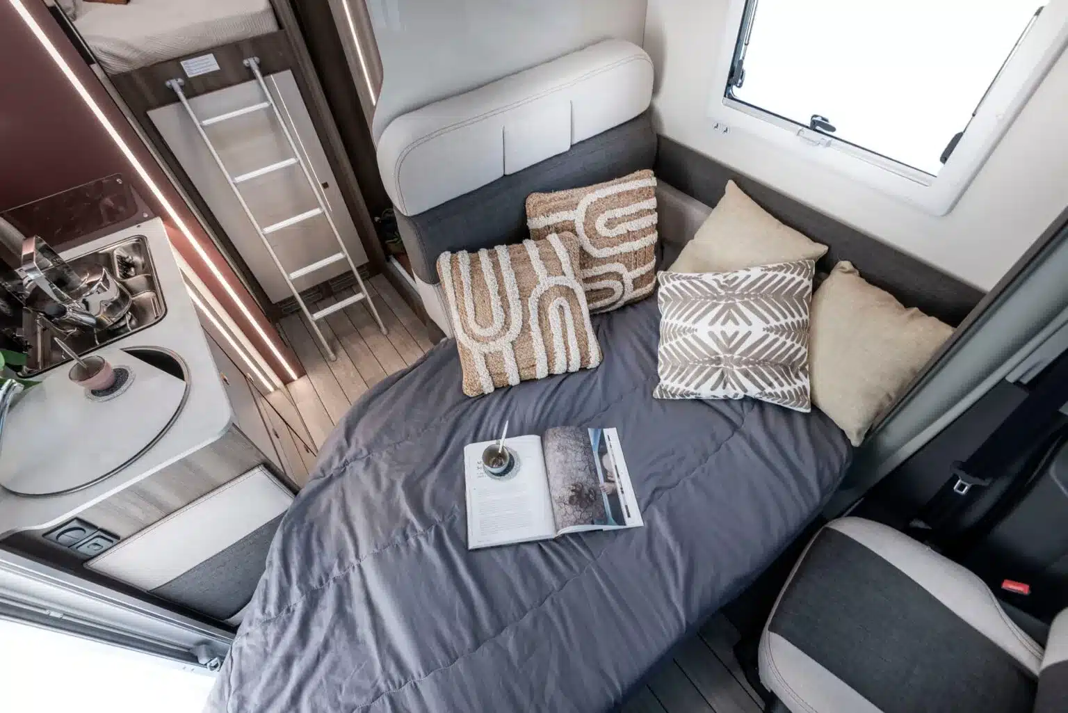 Schlafbereich und Küchenzeile im Kronos Fit Wohnmobil mit Kissen und Buch