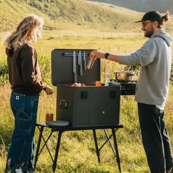 Zwei Menschen kochen an einer Layzee Box Classic Campingküche auf einer Wiese
