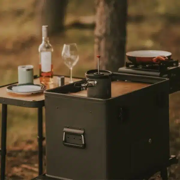 Layzee Box Classic als Campingküche im Freien mit Kochzubehör und gedecktem Tisch.