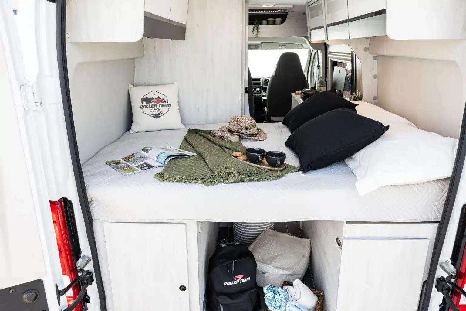 Blick ins Schlafabteil des Livingstone K2 GO Campervans mit aufgeschlagenem Bett, Kissen und Stauraum darunter.
