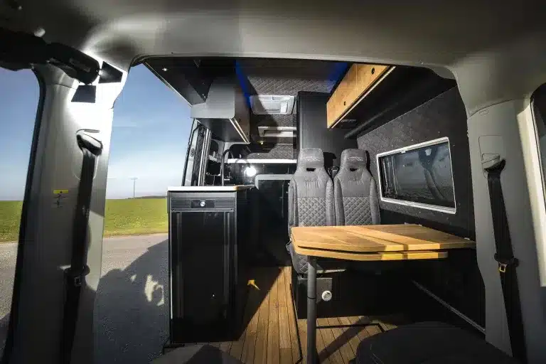 Blick in den Innenraum eines ausgebauten MAN TGE Next Level Reisemobils mit Sitzgruppe und Holztisch.