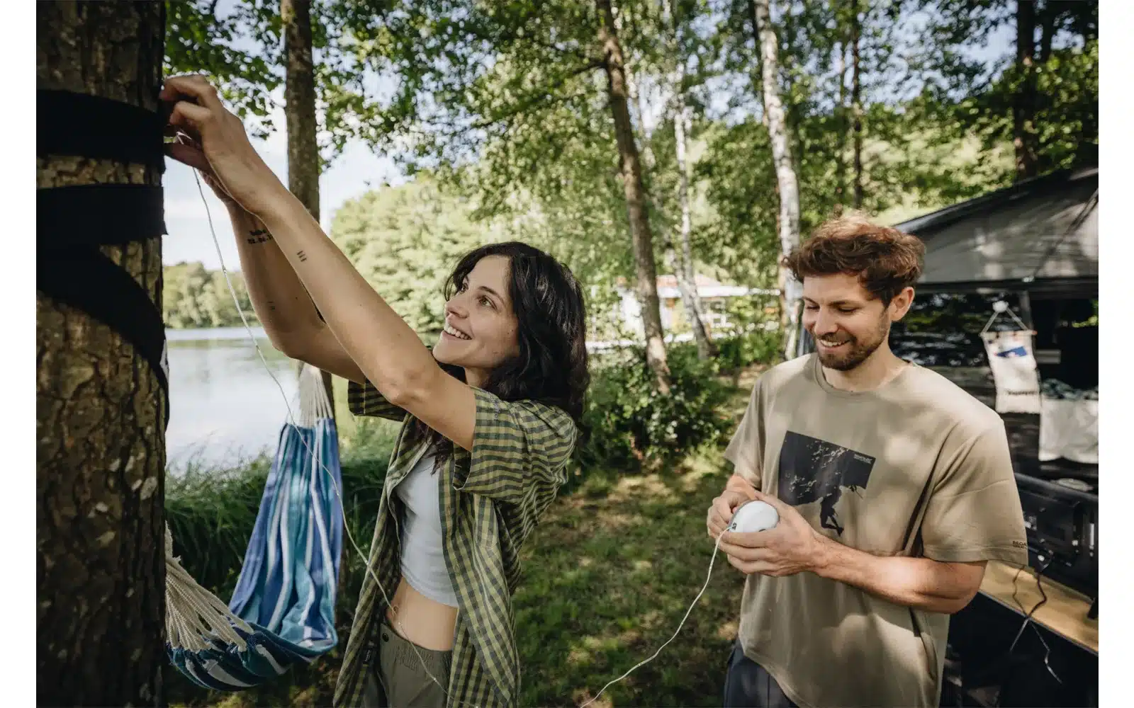 Zwei Menschen montieren eine Berger 2-in-1 Campingleuchte mit Lichterkette am Baum neben einem Campervan.