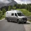 Großer Mercedes Sprinter 7,40 m mit Hochdach und Allradantrieb auf Bergstraße vor Wald und Bergen.