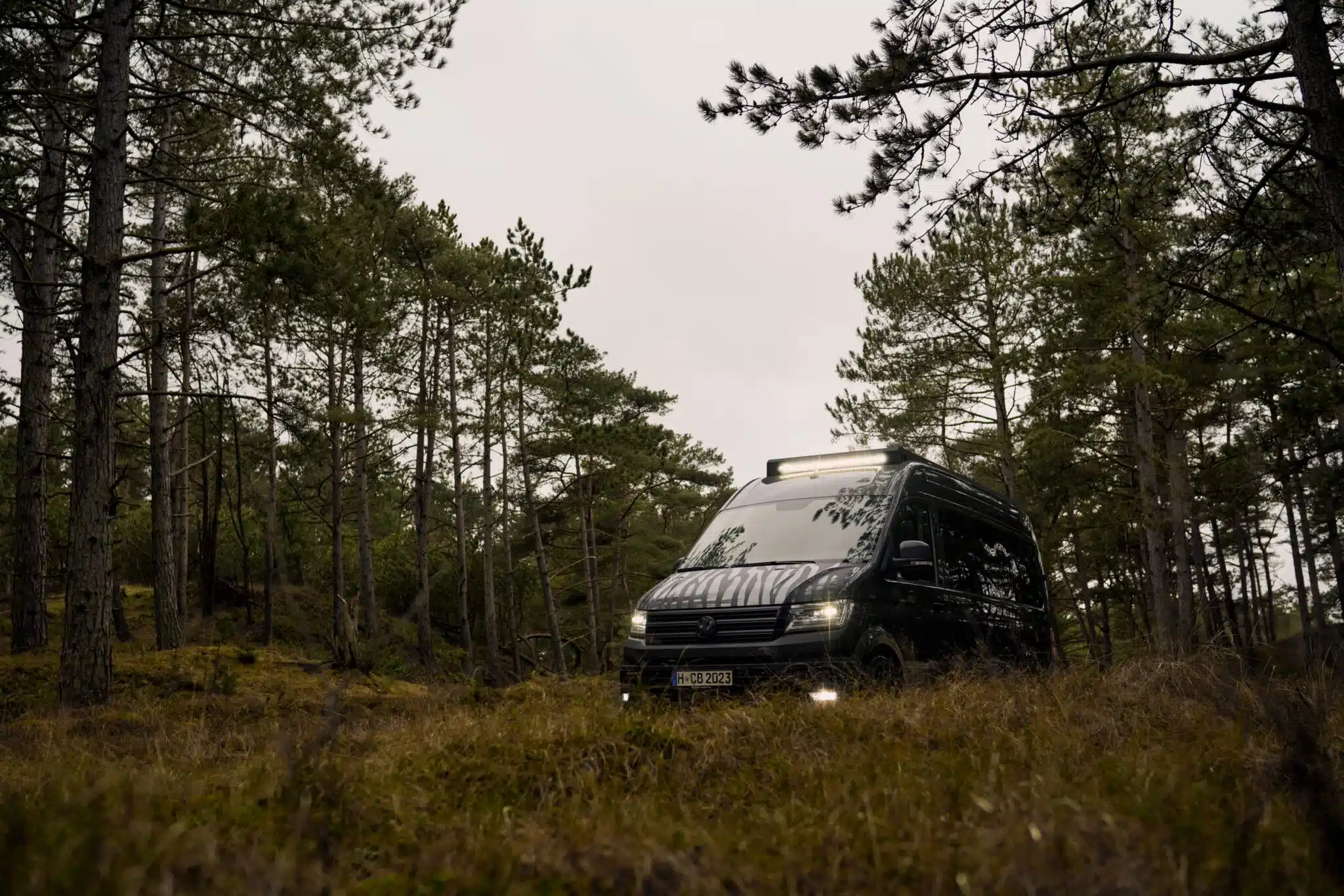 Custom-Bus Camper XL auf Basis Volkswagen Crafter steht im Wald auf unebenem Terrain