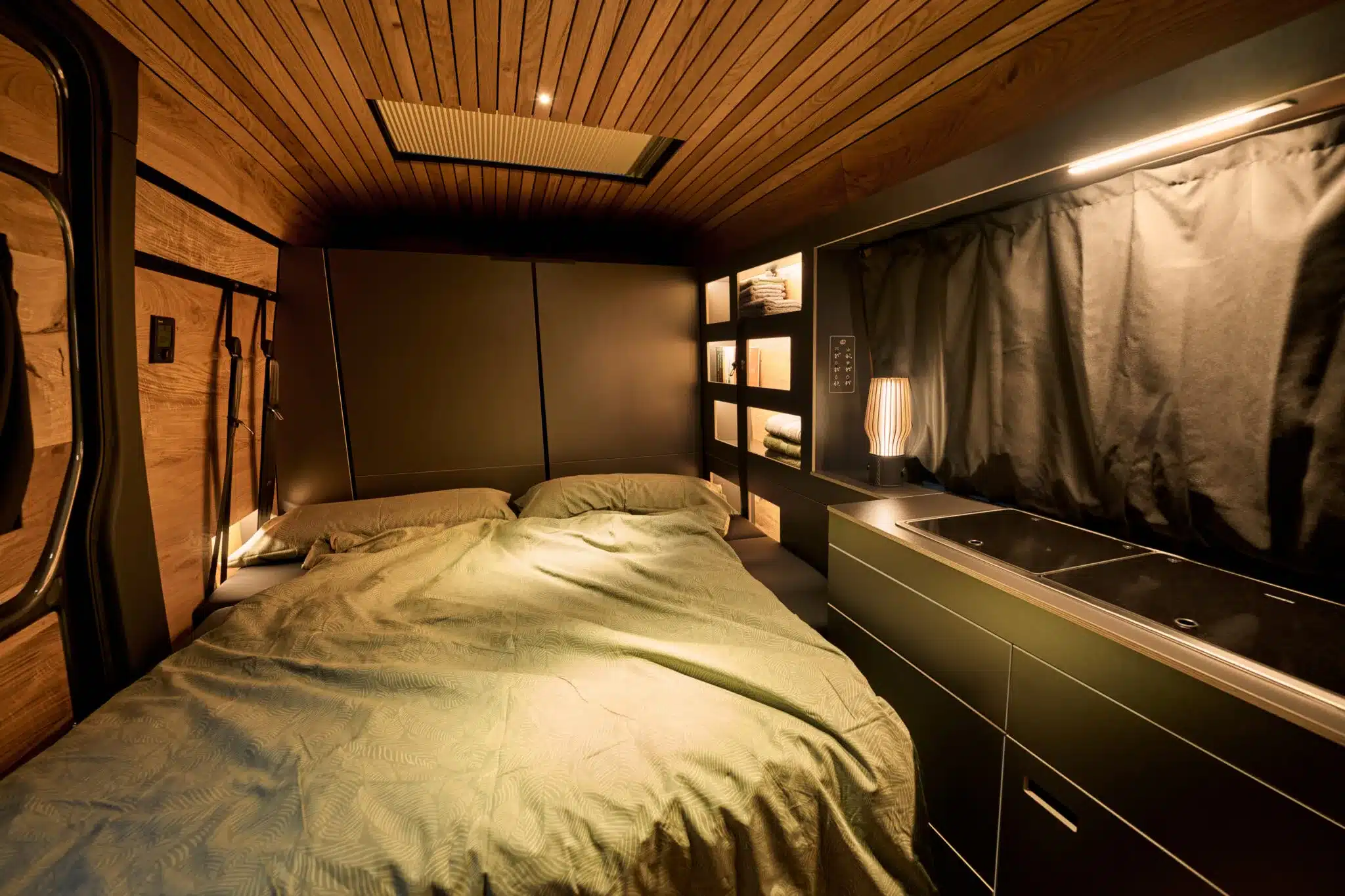 Innenraum des Camper XL auf VW Crafter-Basis mit Doppelbett, Regalen und moderner Küchenzeile.