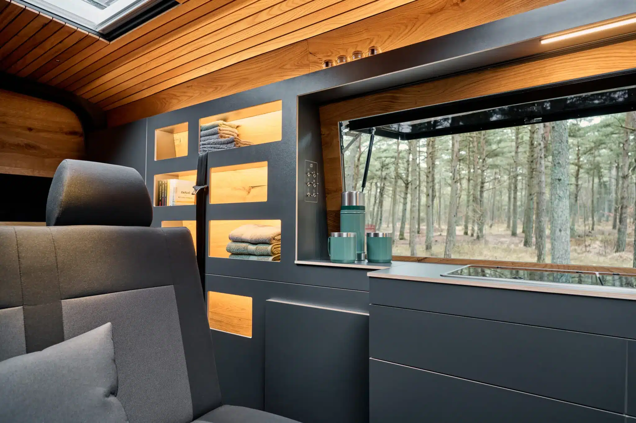 Hochwertiger Innenraum eines Camper-Vans mit Küchenblock, Sitzbank und großem Fenster.