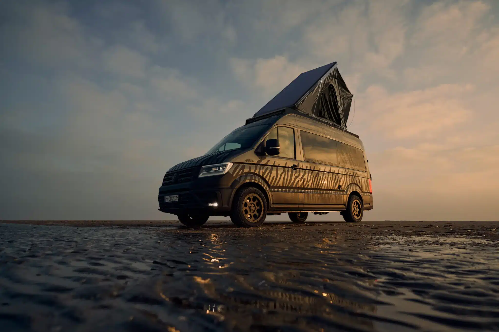 Custom-Bus Camper XL Volkswagen Crafter 2026 mit aufgestelltem Dach auf freier Fläche bei Sonnenuntergang