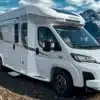 Weißes Progress Lerida Reisemobil auf einer Schotterstraße vor schneebedeckten Bergen.