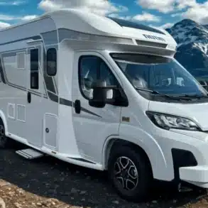 Weißes Progress Lerida Reisemobil auf einer Schotterstraße vor schneebedeckten Bergen.