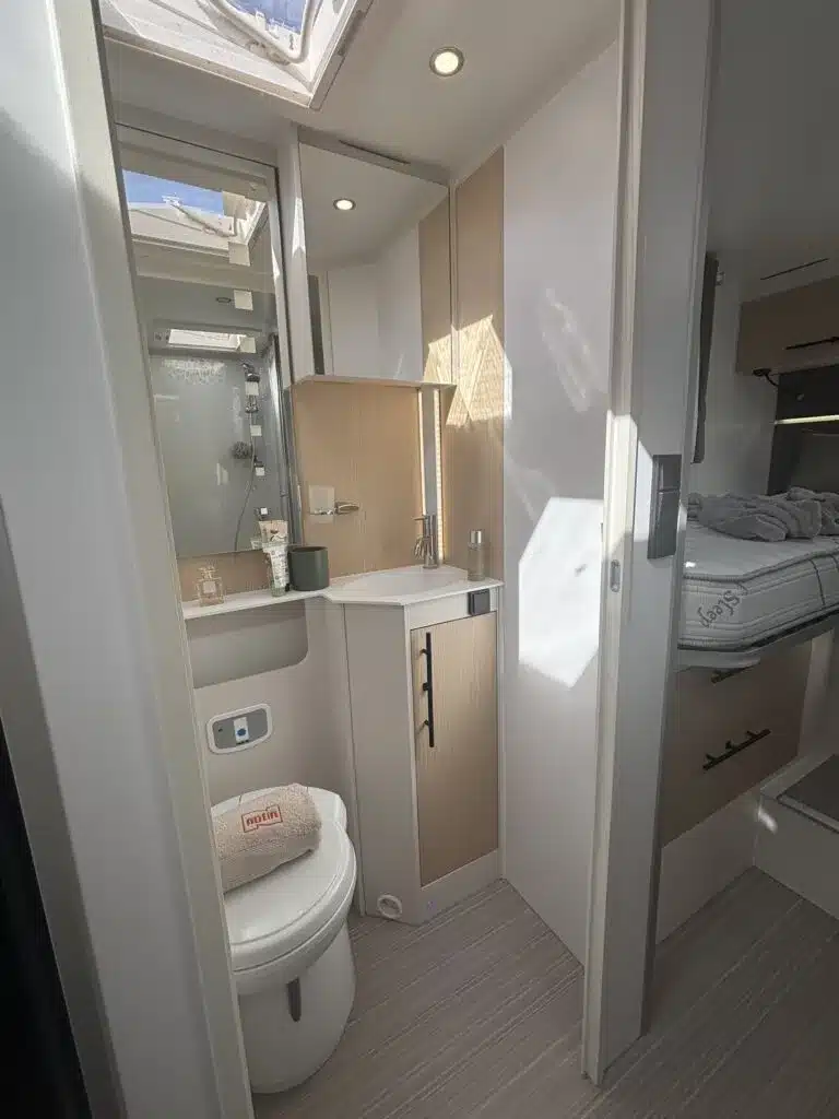 Modernes Badezimmer mit Toilette und Waschbecken im Progress Lerida Reisemobil, Blick ins Schlafzimmer.