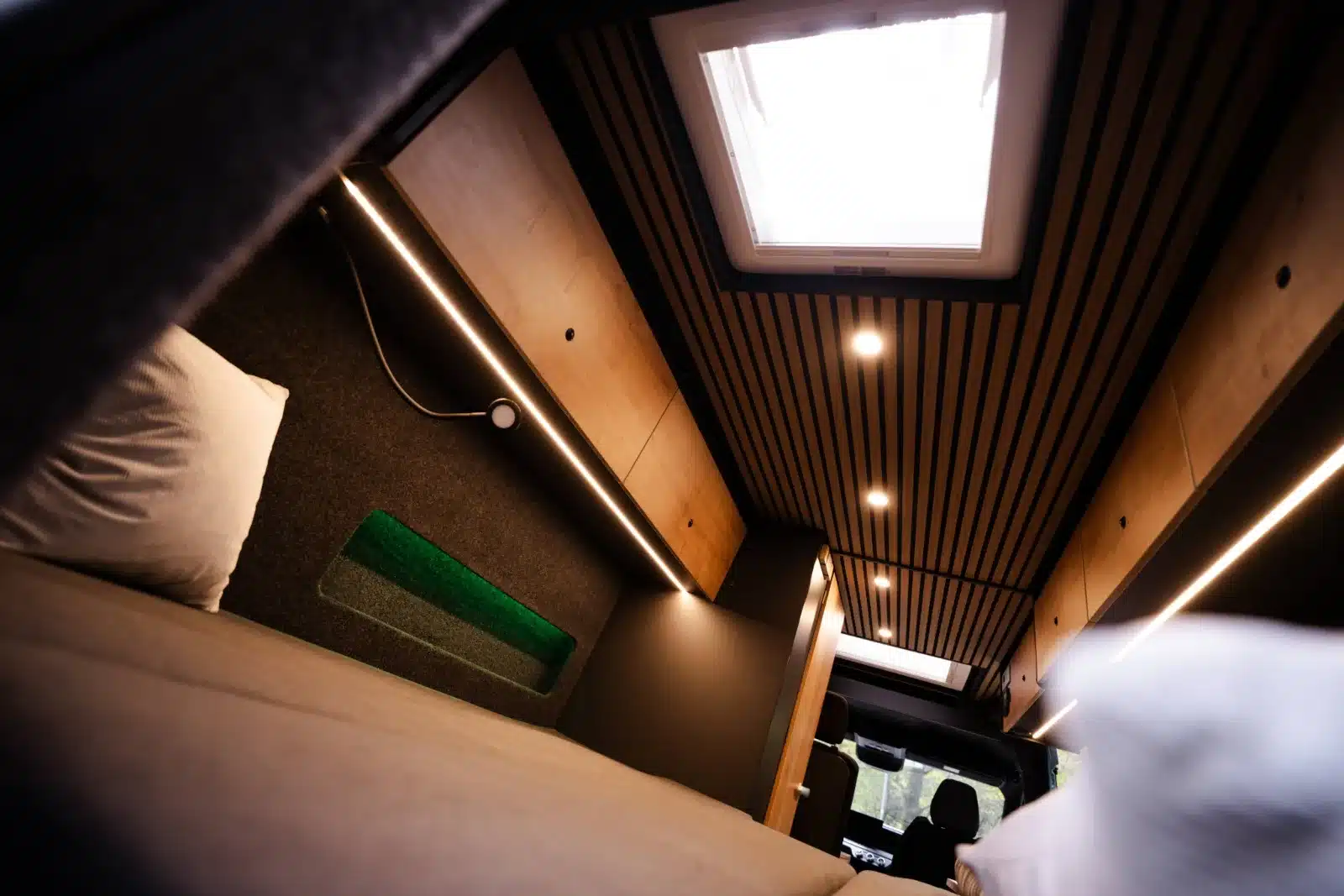 Innenansicht des Renault Master VANtastic zeigt das Längsbett, Oberschränke, Holzverkleidung und LED-Beleuchtung.