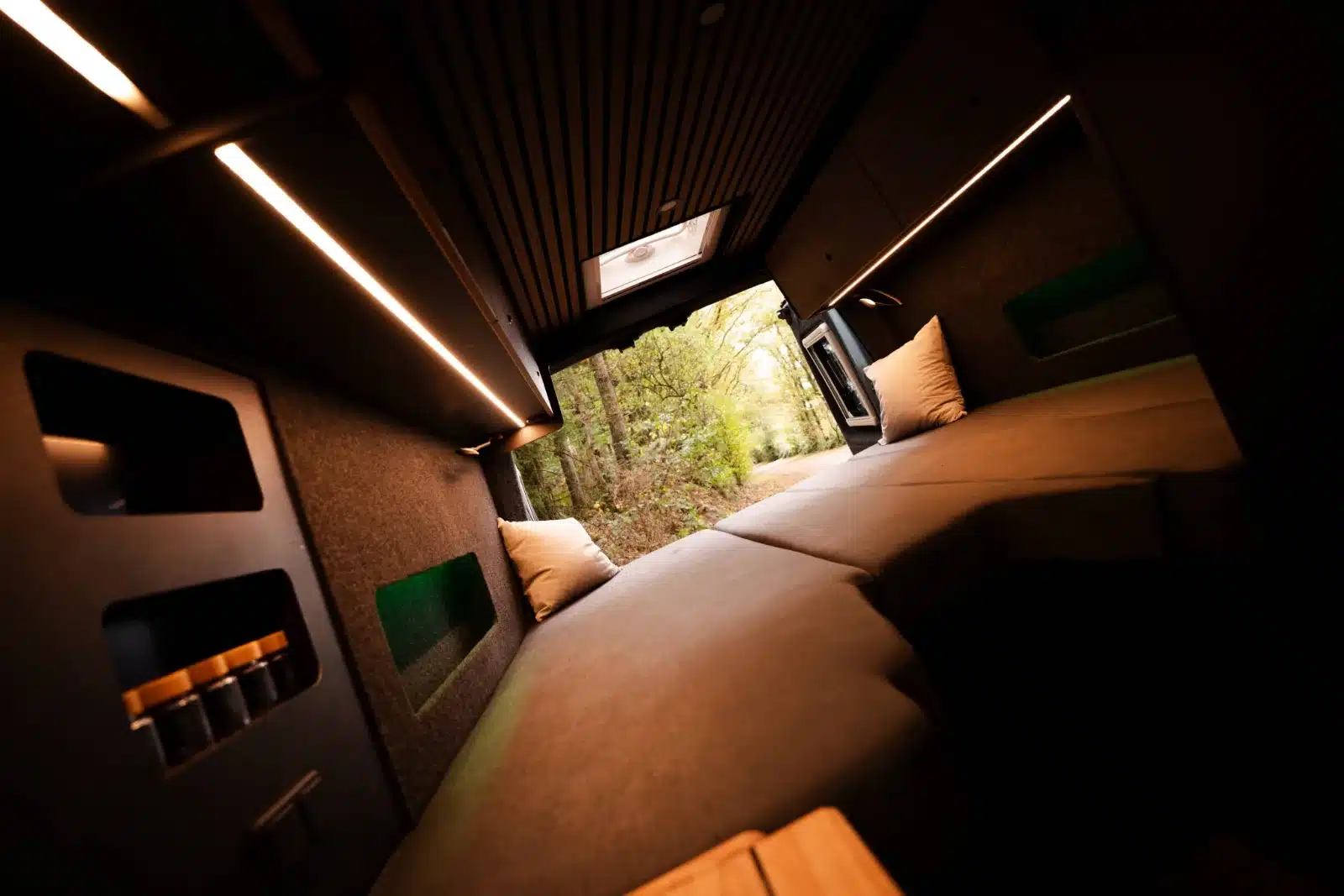 Innenansicht des Renault Master VANtastic mit Längsbett, beleuchteten Schränken und Ausblick nach draußen.