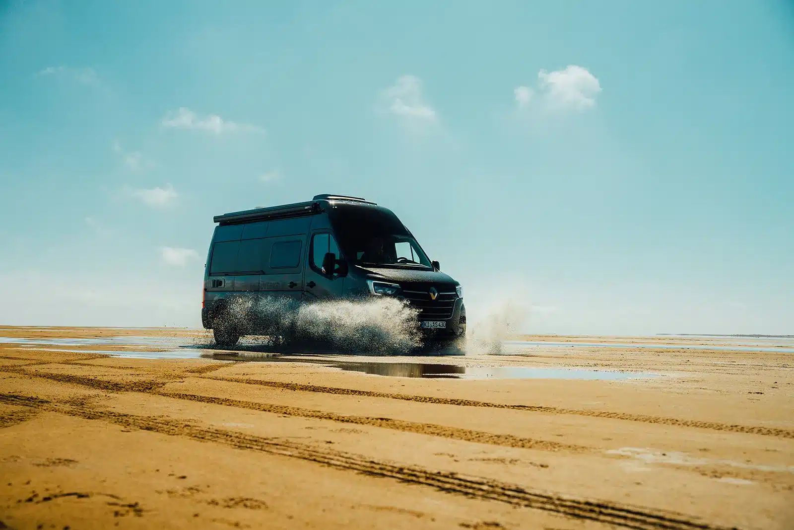 Der Renault Master VANtastic fährt am Strand durch Wasser bei sonnigem Himmel.